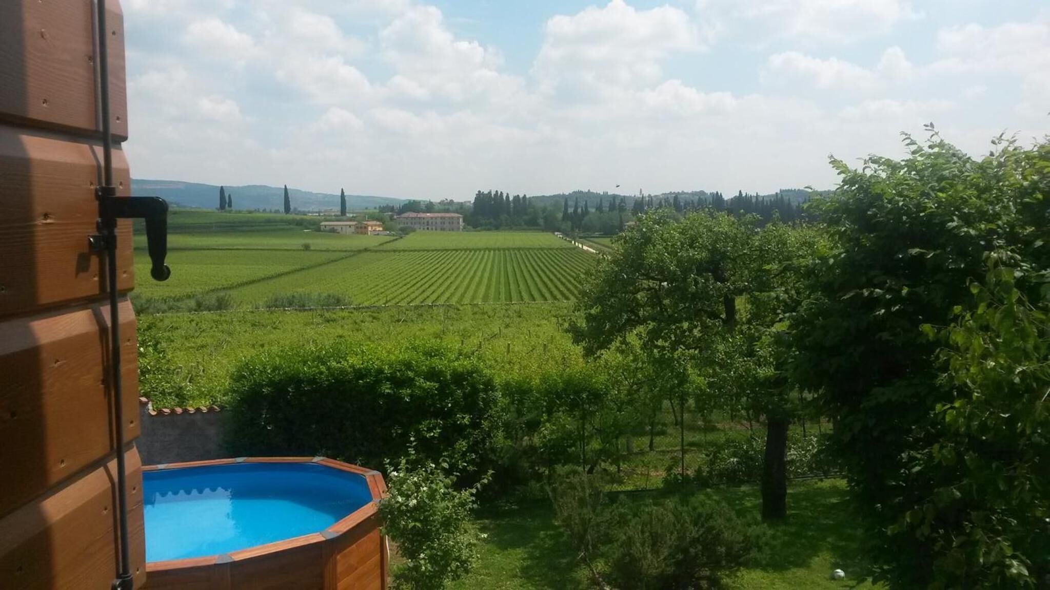 A view from a room with a wooden pool, overlooking a vineyard and distant buildings.
