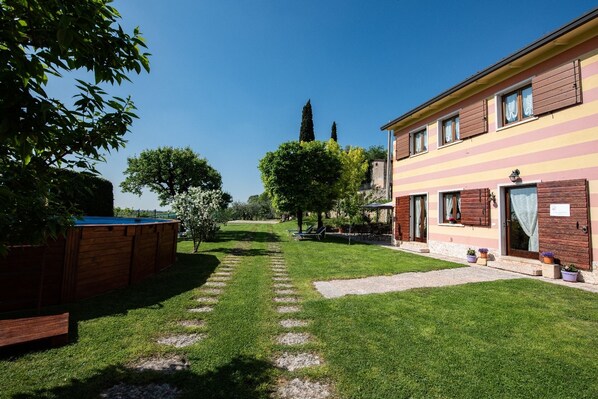 A courtyard with a swimming pool, a wooden deck, and a building with striped walls and windows. - Agriturismo El Crear (San Pietro in Cariano)