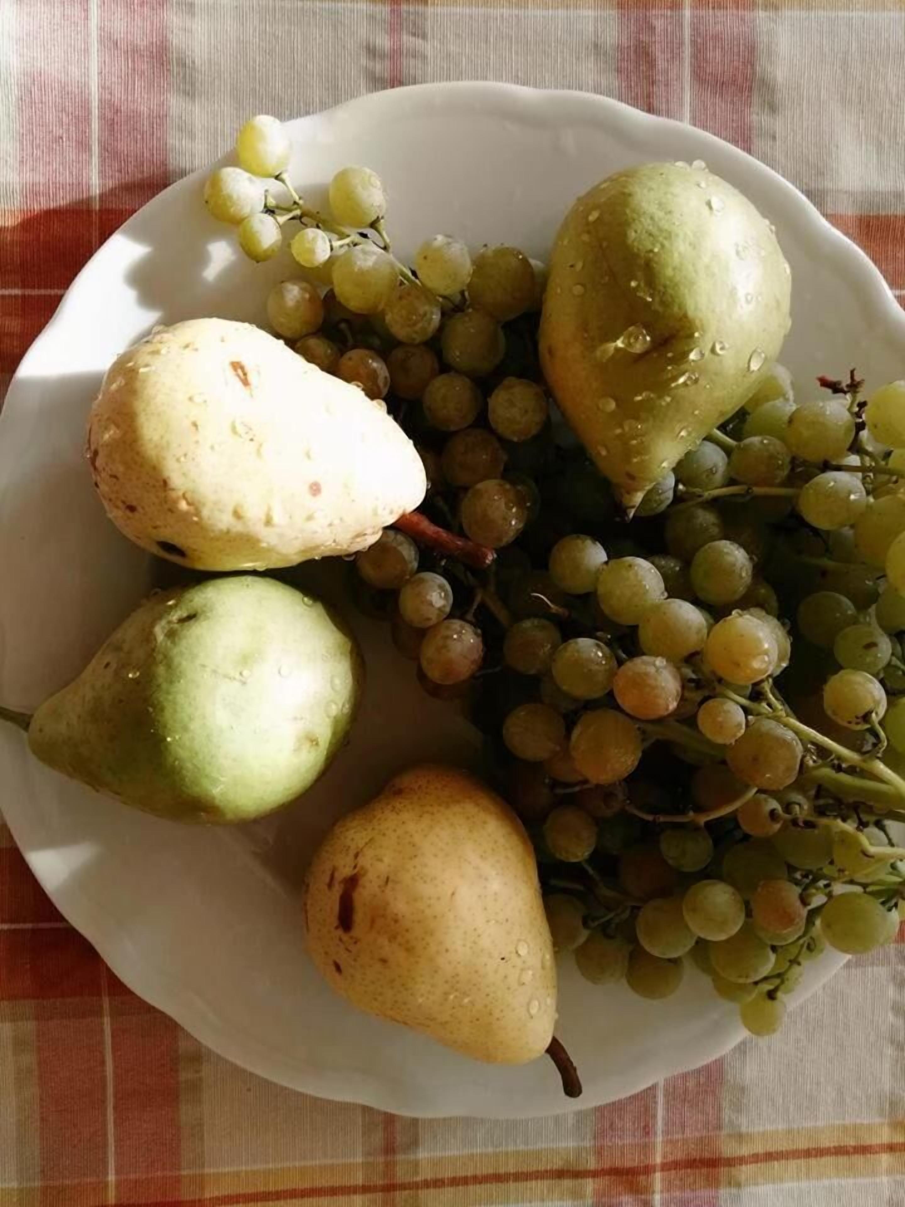 Un plato con peras y uvas sobre un mantel.