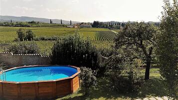 A swimming pool surrounded by a garden with a view of a vineyard and distant hills.