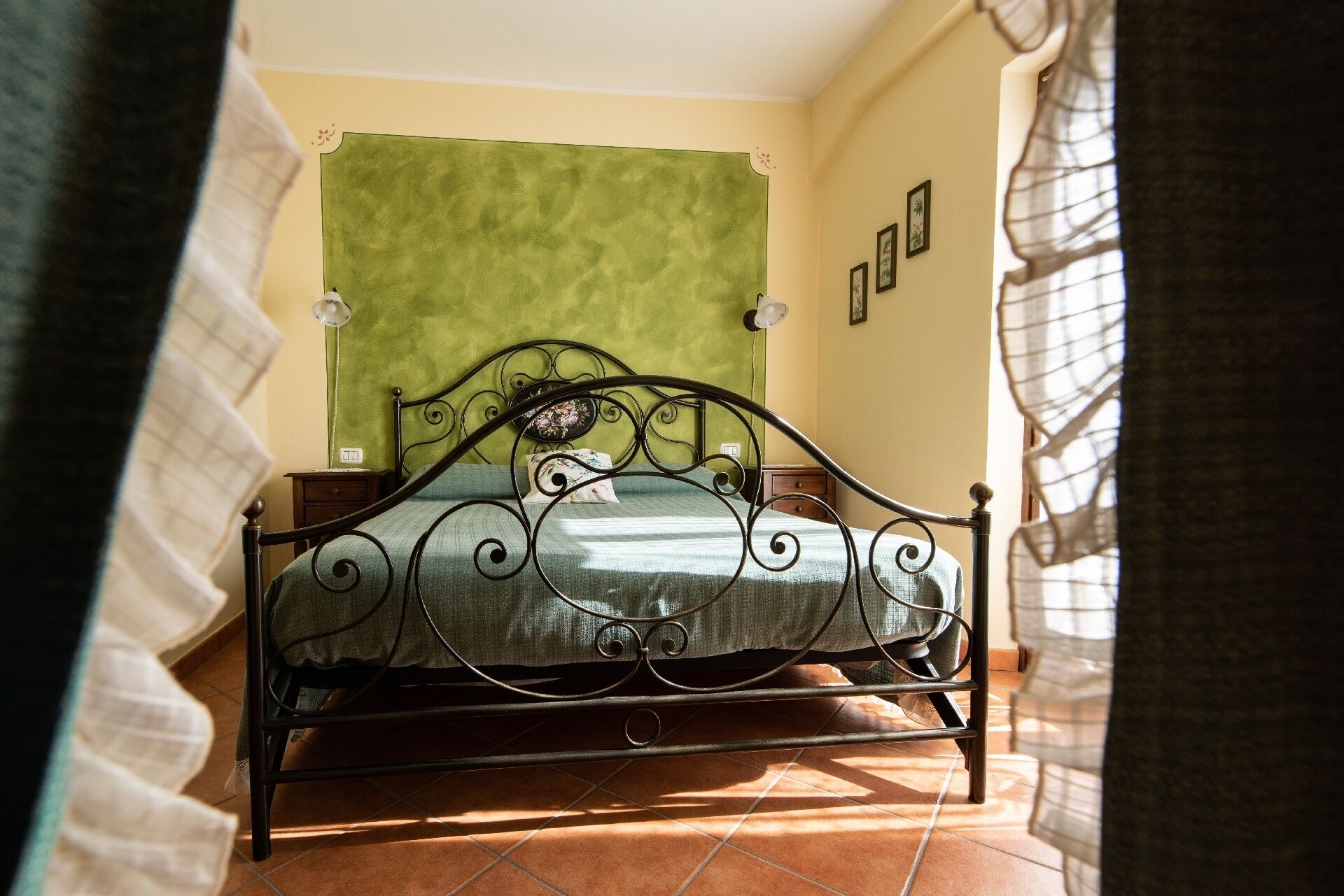 Una cama con cabecera verde en una habitación con suelo de baldosas y una pared decorada con cuadros.