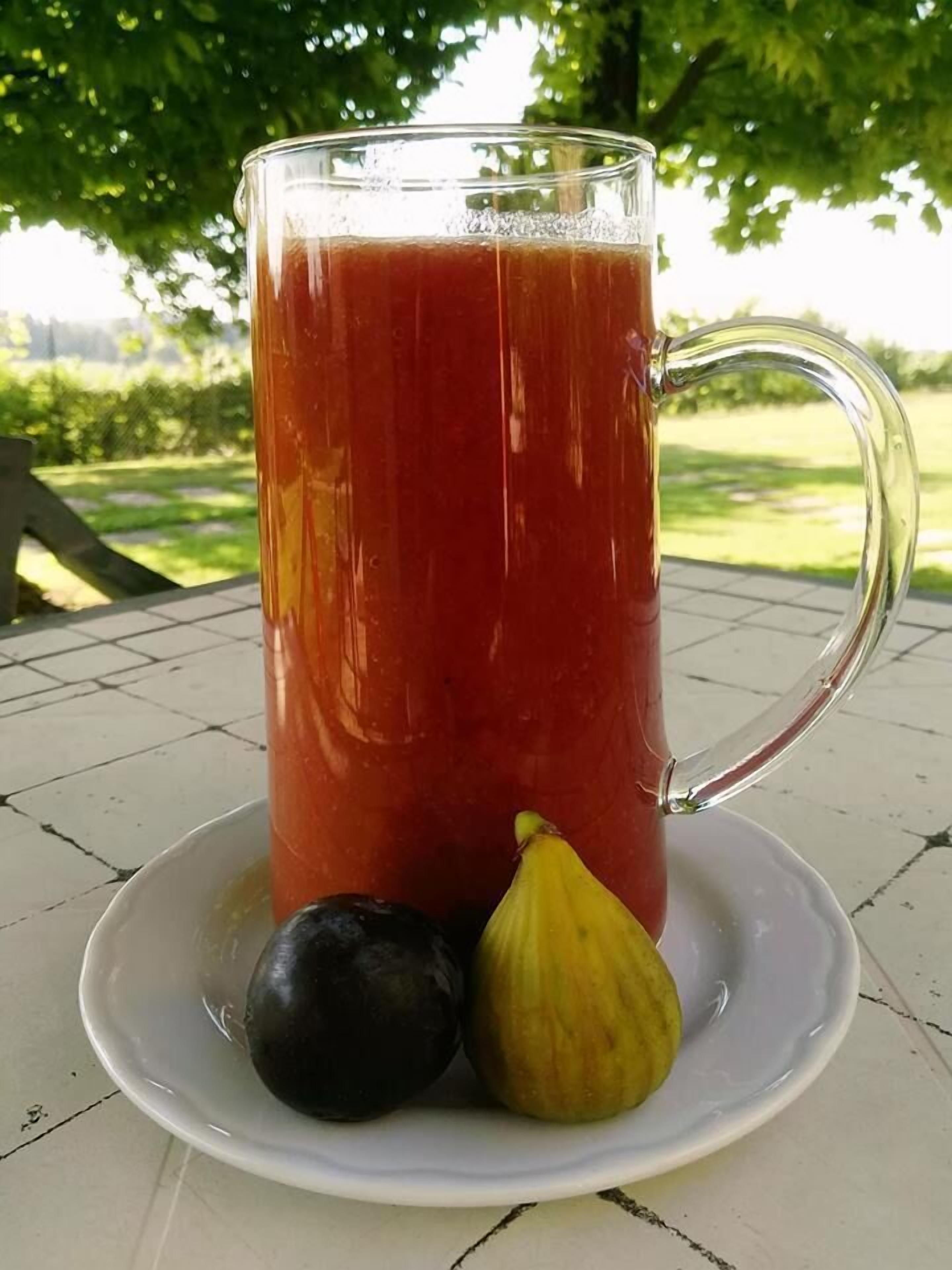 A tall glass mug filled with a red beverage, placed on a white plate with two fruits beside it.