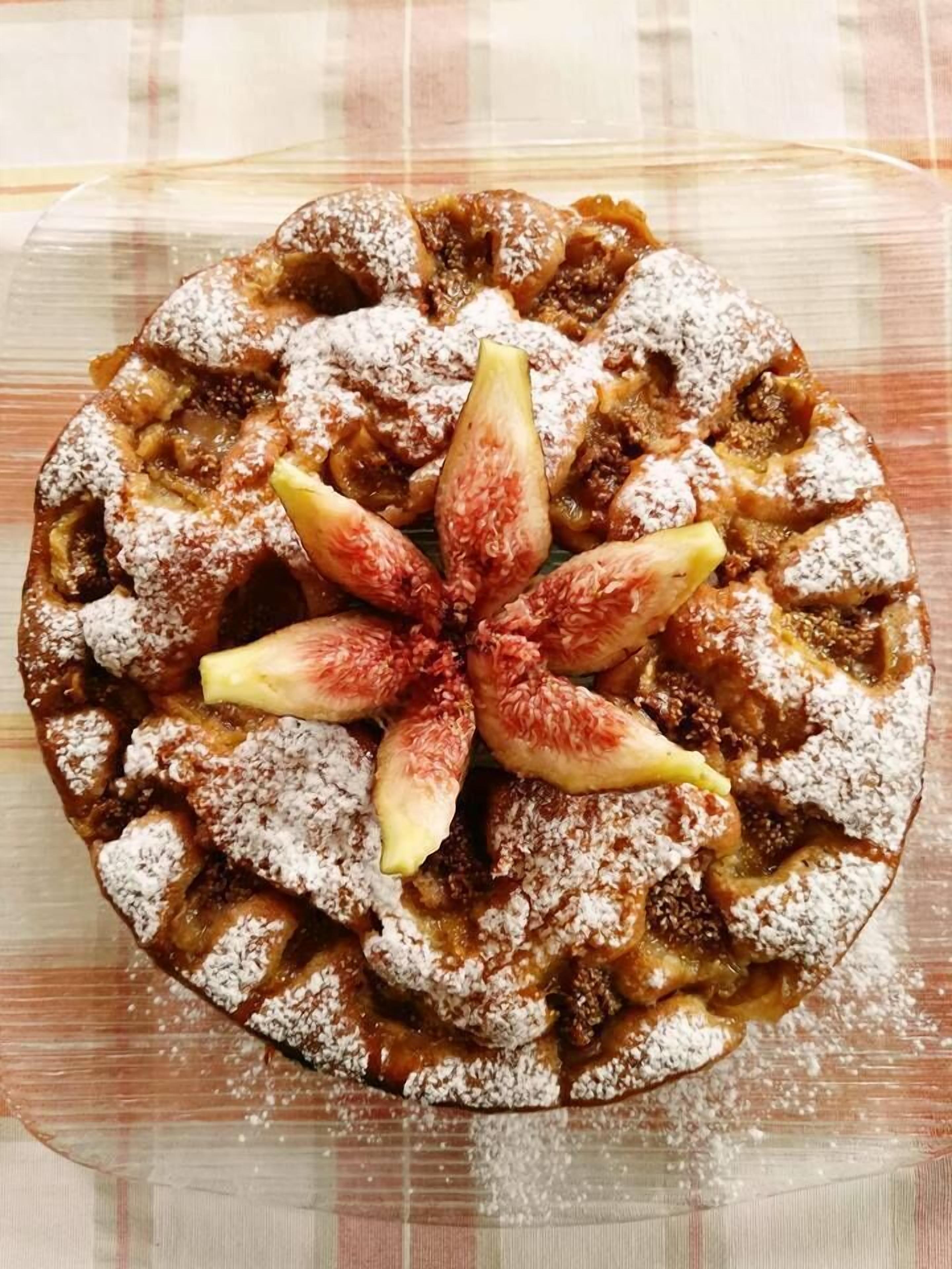 A round dessert topped with sliced figs and powdered sugar.