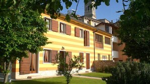 A two-story building with a yellow facade, multiple windows with wooden shutters, and a stone wall at the base. - Agriturismo El Crear (San Pietro in Cariano)
