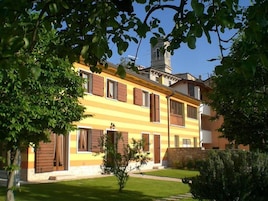A two-story building with a yellow facade, multiple windows with wooden shutters, and a stone wall at the base.