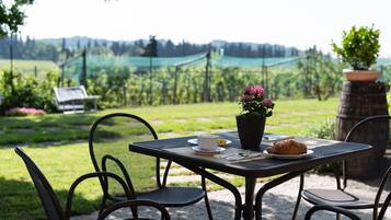 Una mesa al aire libre con sillas, una planta en maceta, un croissant y una taza de café.