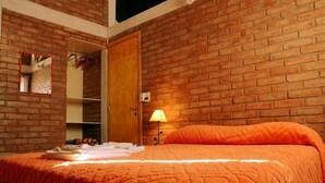 Ein Schlafzimmer mit Backsteinwand, einer Holztür, einem Bett mit orangefarbener Decke, einem Nachttisch und einer Lampe.