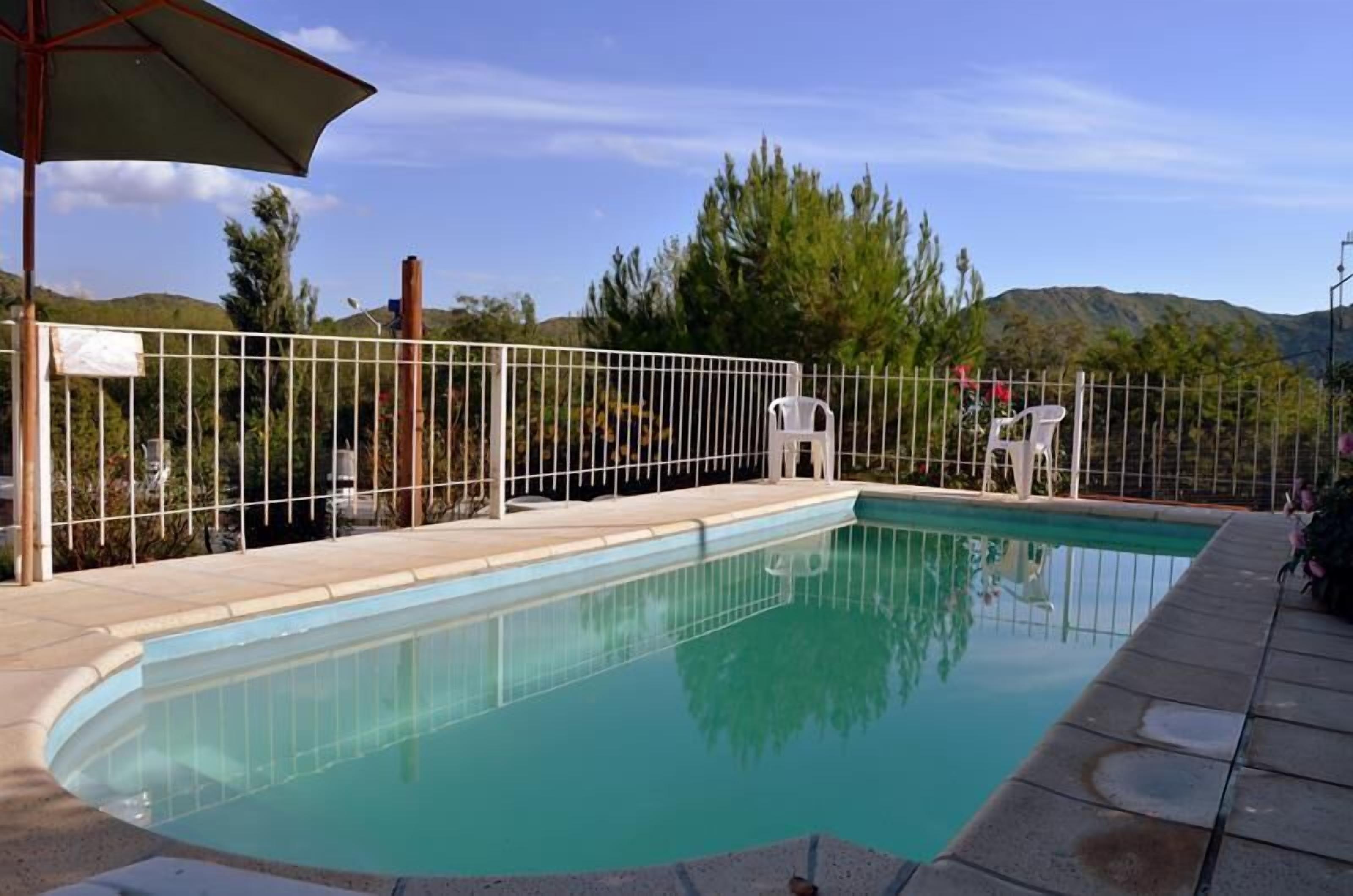 A swimming pool with a white fence, a covered area, and a view of trees and hills in the background.