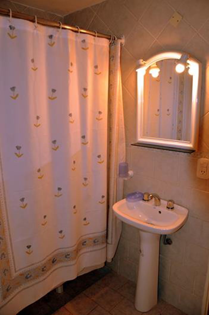 Un baño con un lavamanos blanco, un espejo con iluminación y una cortina de ducha estampada.