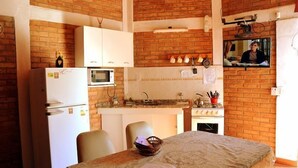Eine kleine Küche mit Kühlschrank, Mikrowelle und Herd. Ein Esstisch mit Stühlen und einem Korb steht daneben.