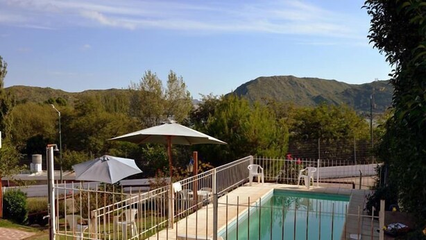 Ein Pool mit umzäuntem Deck, Liegestühlen im Freien und einem überdachten Bereich mit Sonnenschirm.