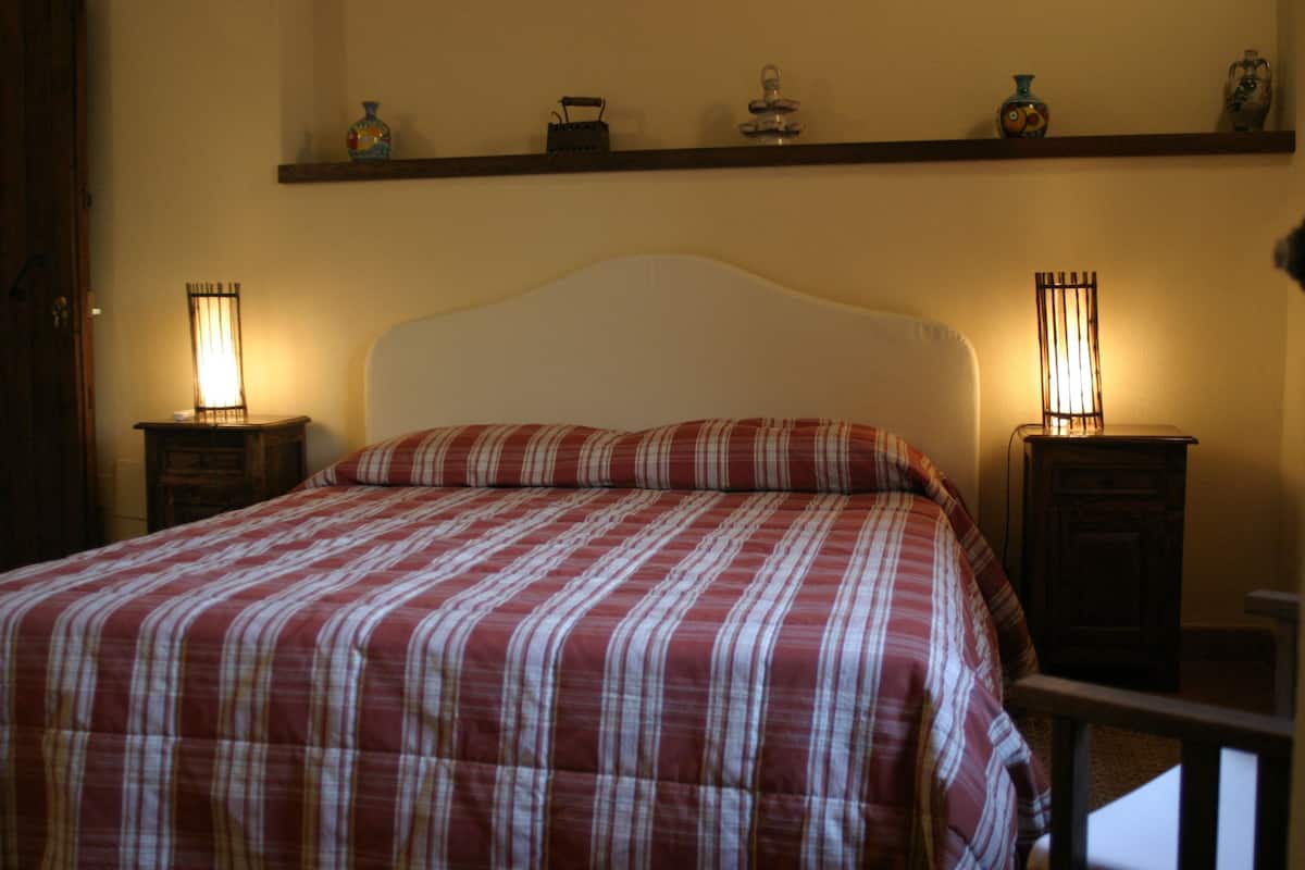 A bed with a plaid bedspread, two bedside tables with lamps, and a shelf above the bed with decorative items.