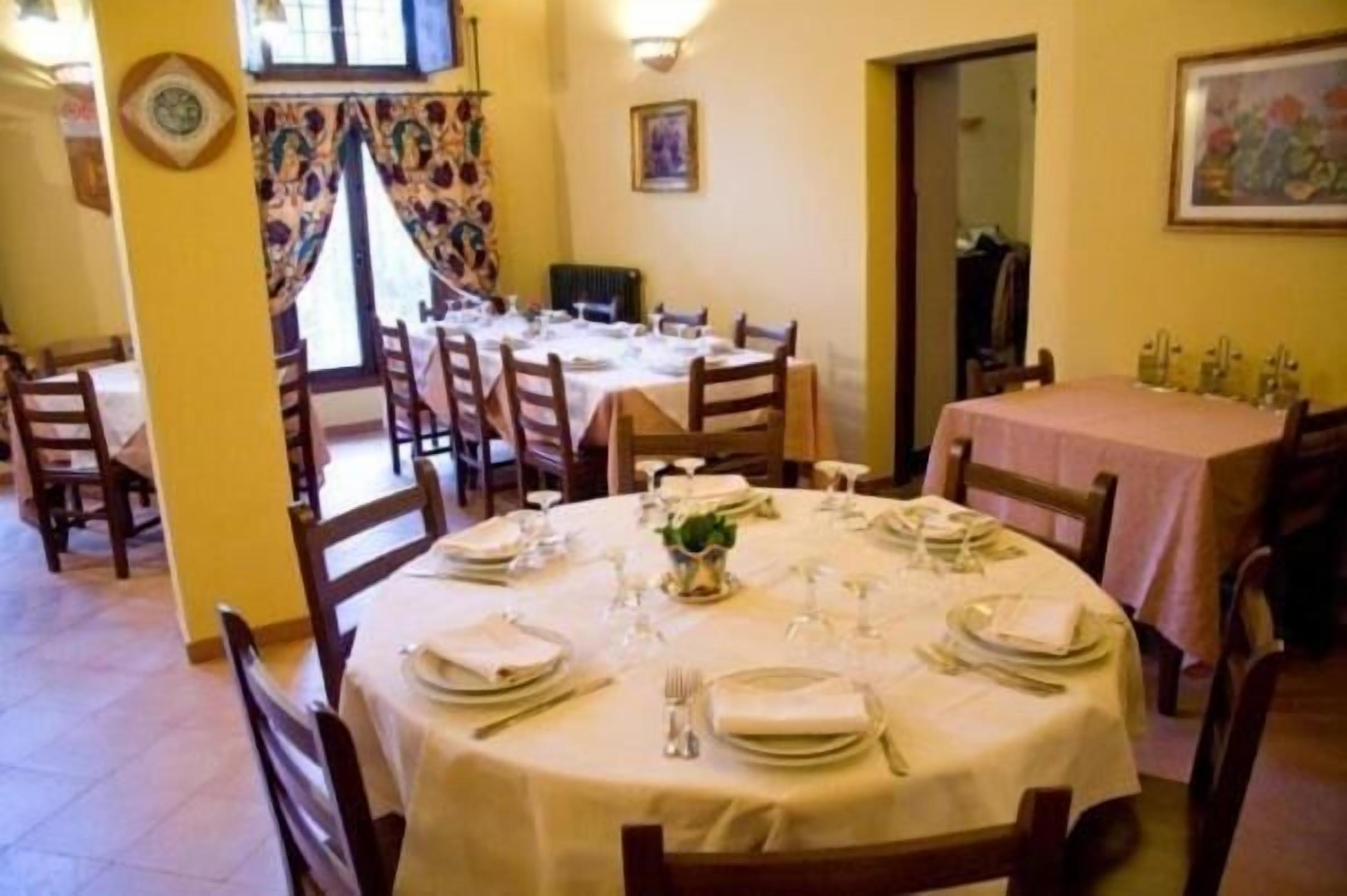 A dining area with round tables set for a meal, chairs, and a window with curtains.
