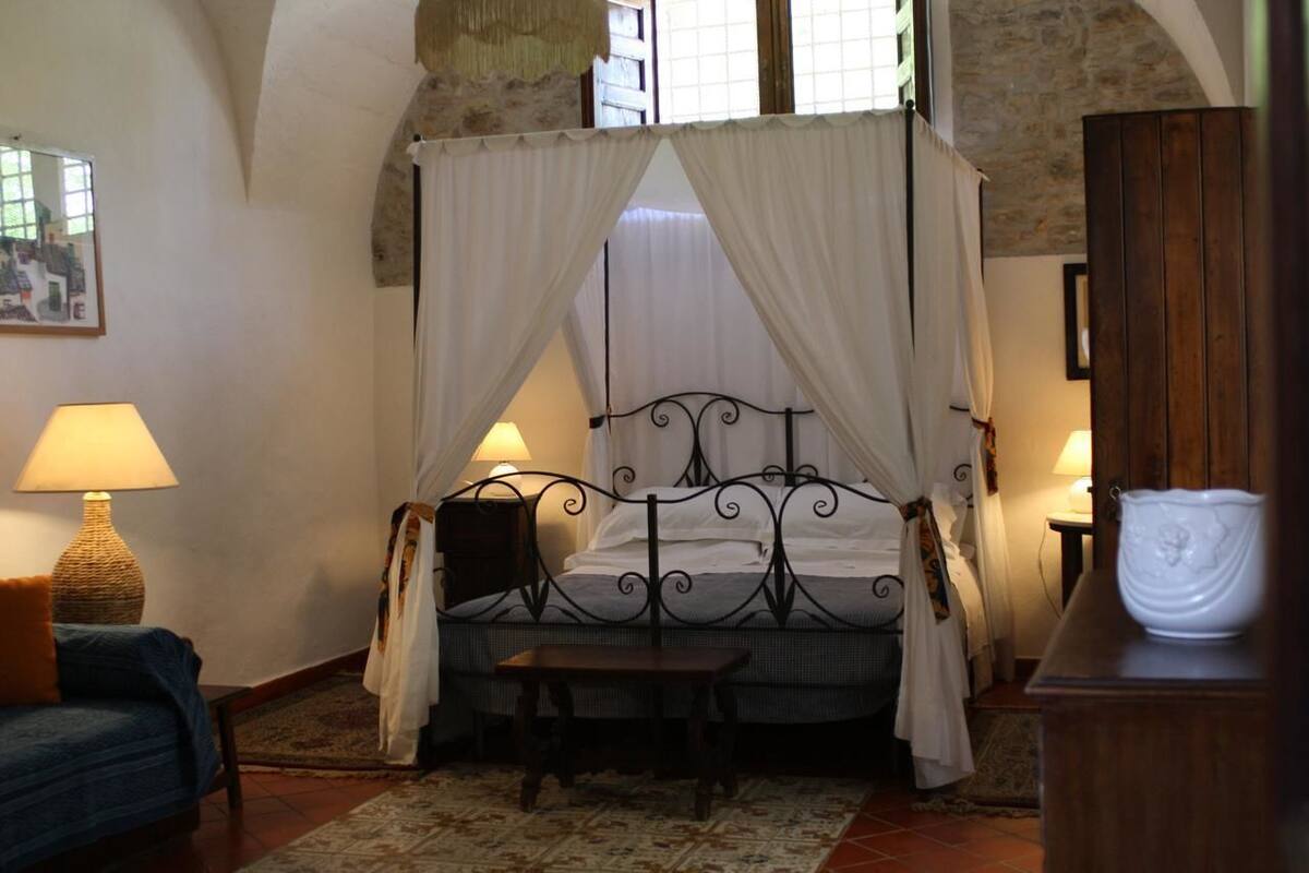 A bedroom with a four-poster bed, a nightstand, a lamp, a chair, and a cabinet.