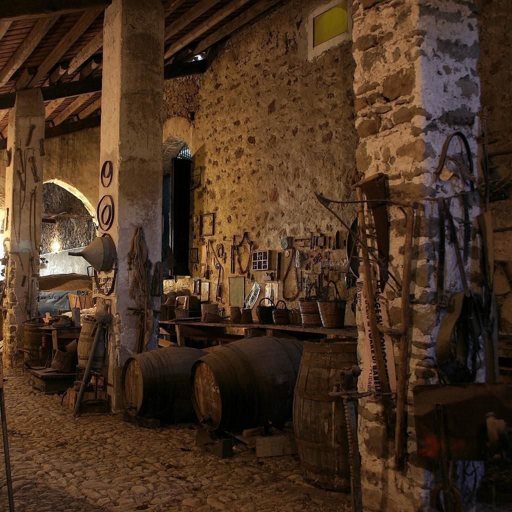 A rustic cellar with stone walls, wooden barrels, and various tools.