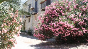 A stone building with balconies, surrounded by flowering bushes and a palm tree. - Ridocco Agriturismo (Campofiorito)