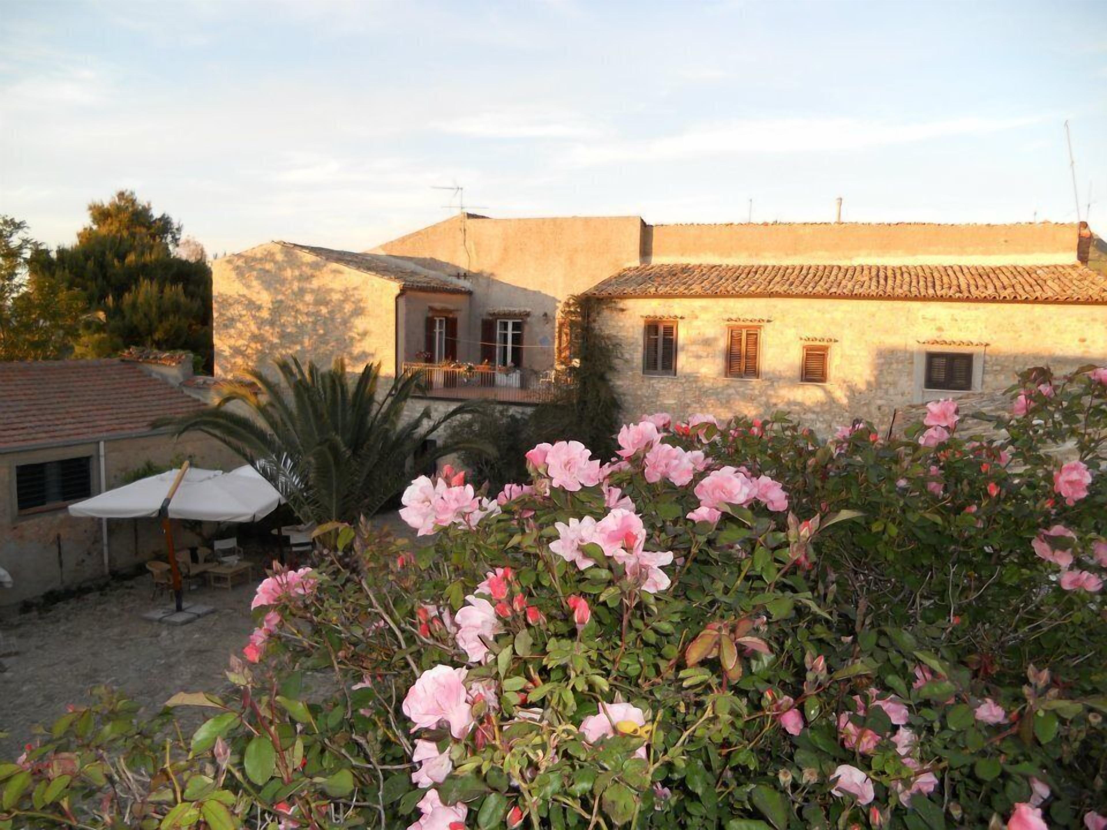 Un edificio rustico con tetto in tegole, un balcone e un giardino con fiori rosa.