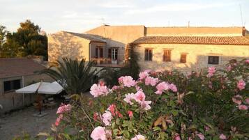 Un edificio rustico con tetto in tegole, un balcone e un giardino con fiori rosa.