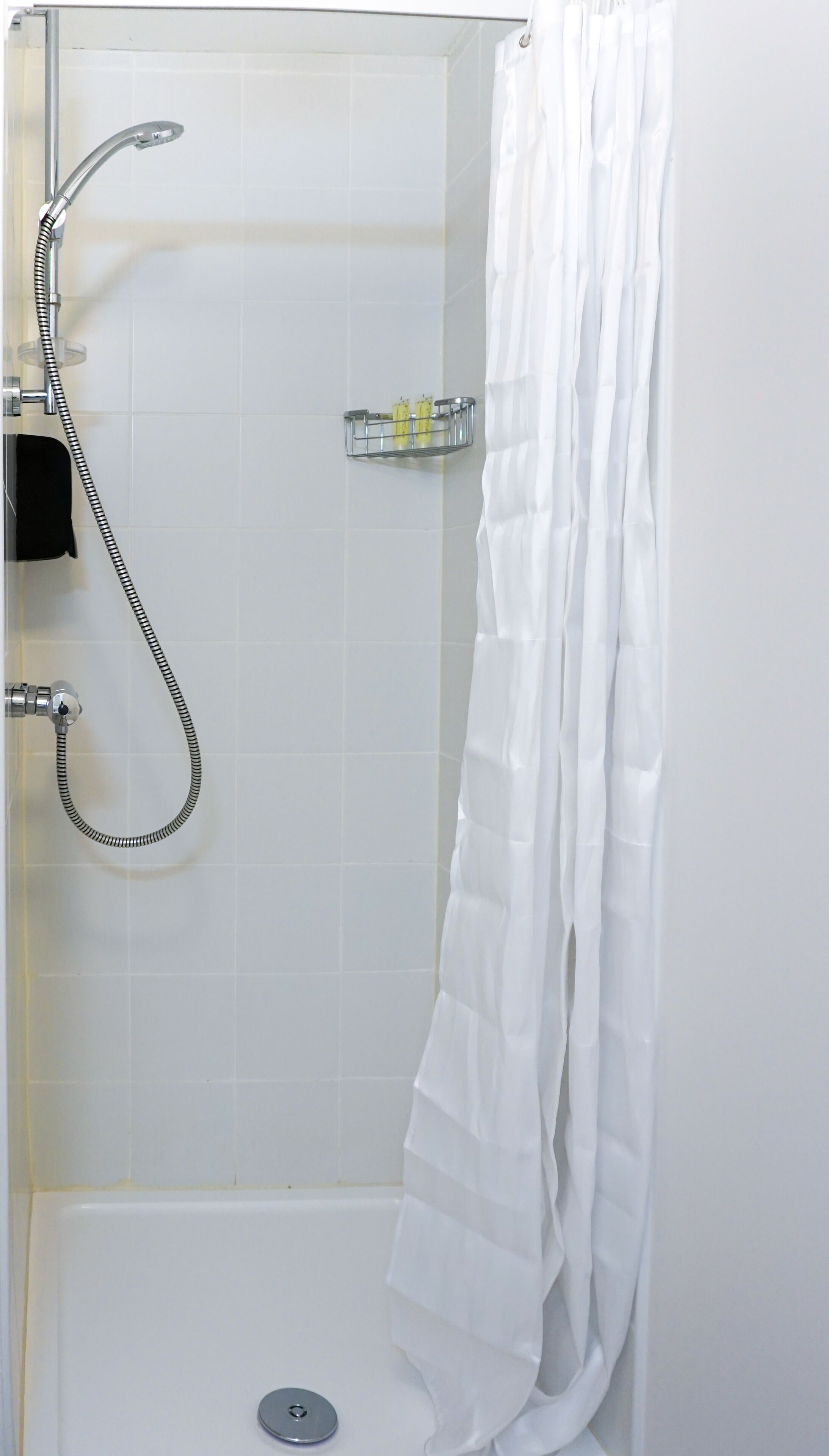 A shower area with a white curtain, a handheld showerhead, and a wall-mounted faucet.