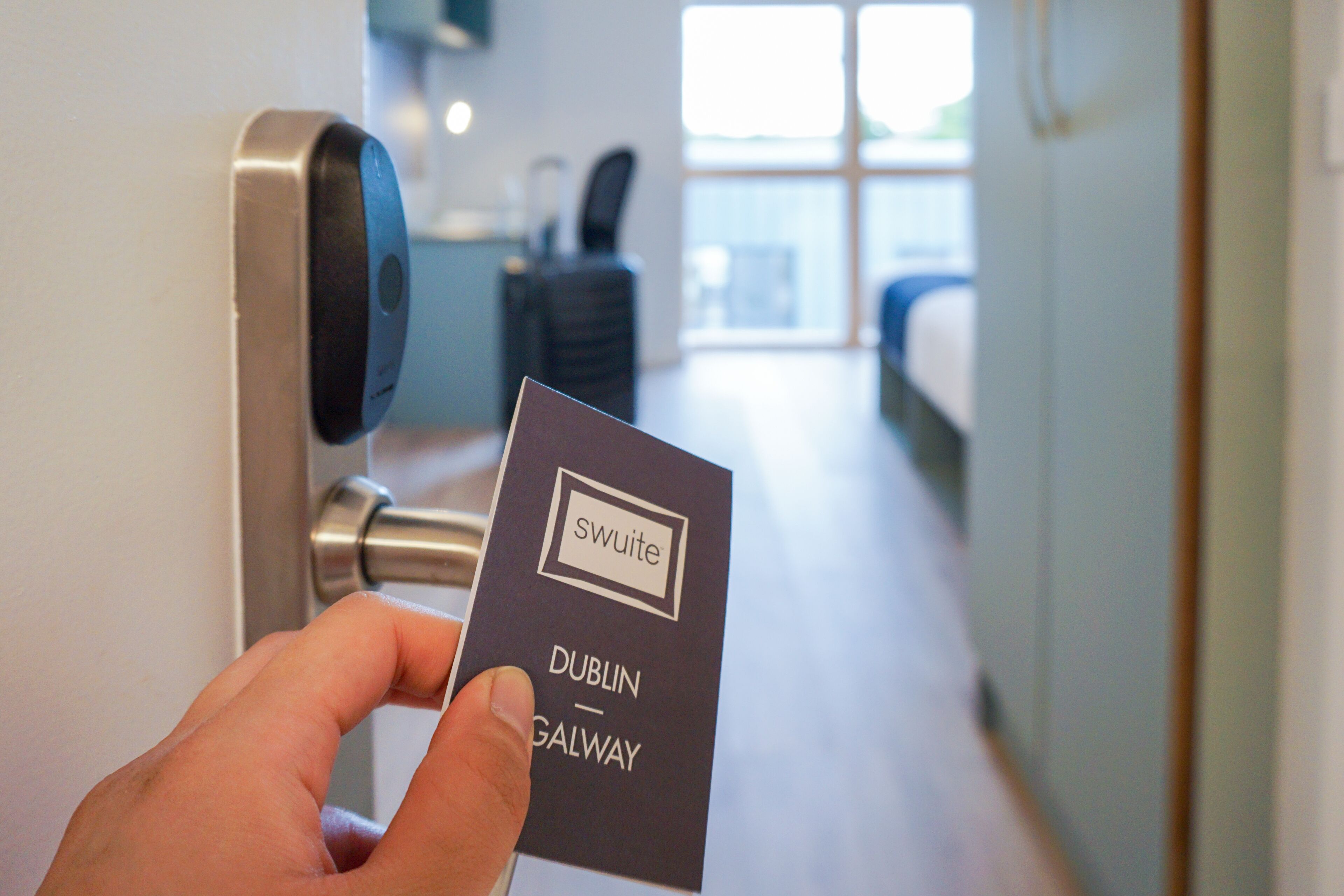 A hand holding a card with "swuite" and "Dublin Galway" written on it, in front of a door with a keypad lock.