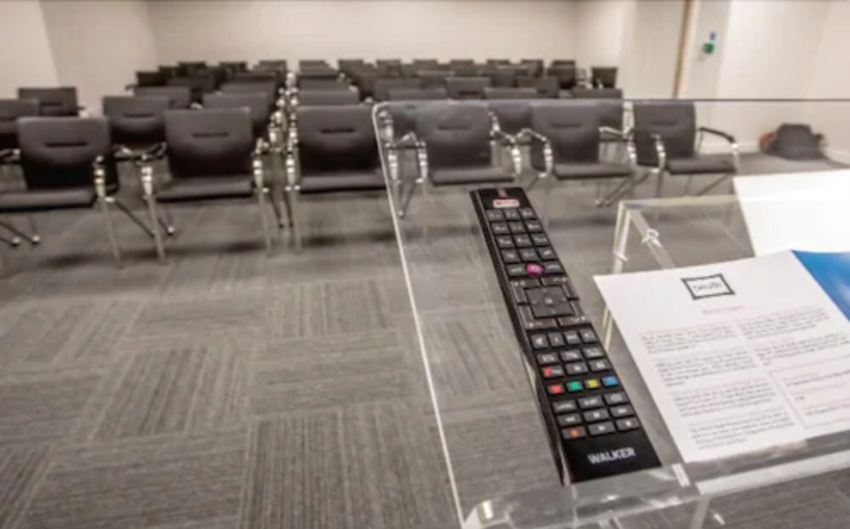 A conference room with rows of chairs and a podium with a remote control.