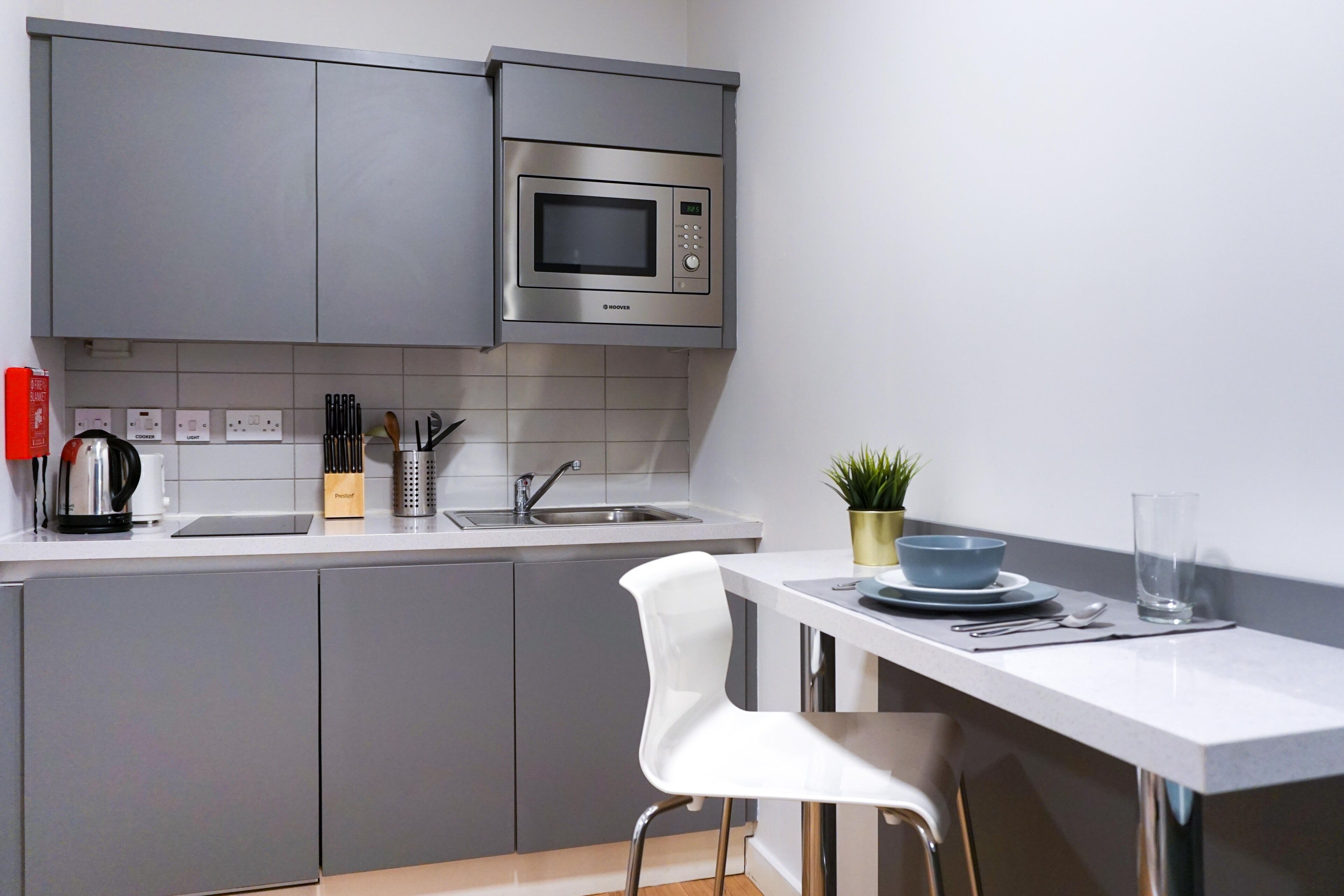 Cozinha moderna com armários cinza, micro-ondas de aço inoxidável, pia e um banquinho branco.