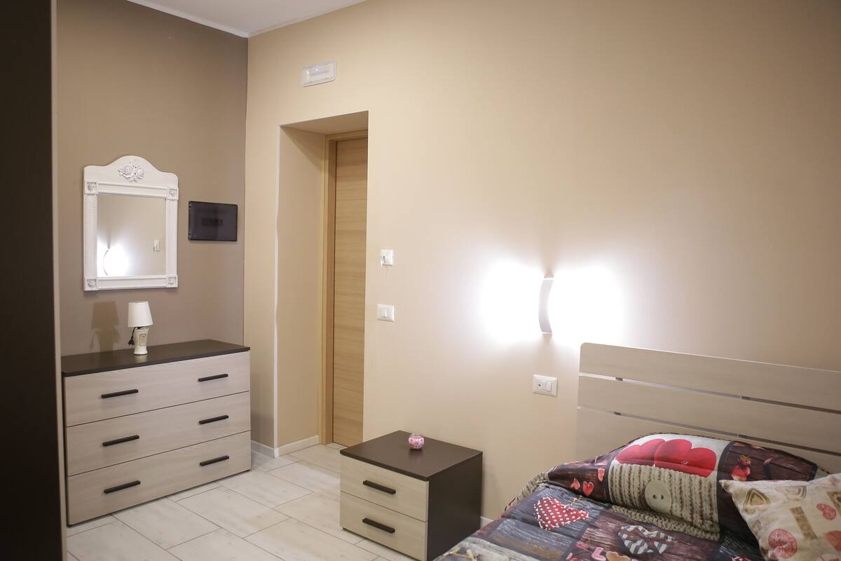 A bedroom with a bed, a dresser, a mirror, and a small table.