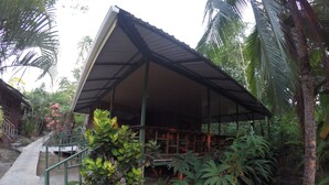 A covered outdoor seating area with a concrete path leading to it, surrounded by lush greenery and palm trees. - Jonny's cabins drake day (Drake Bay)