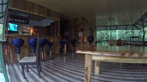 A wooden interior with a bar area, bar stools, and a large table. - Jonny's cabins drake day (Drake Bay)