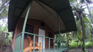 A small, single-story house with a porch and a chair, surrounded by lush greenery. - Jonny's cabins drake day (Drake Bay)