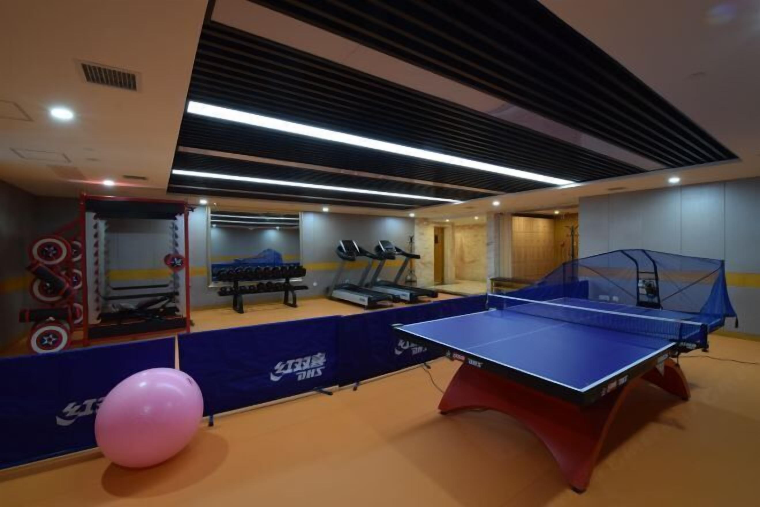 Een fitnessruimte met trainingsapparatuur, een tafeltennistafel en een roze fitnessbal.