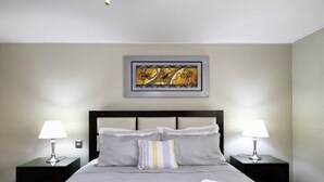 Una cama bien hecha con colcha y almohadas grises, dos lámparas de noche y una obra de arte enmarcada en la pared.