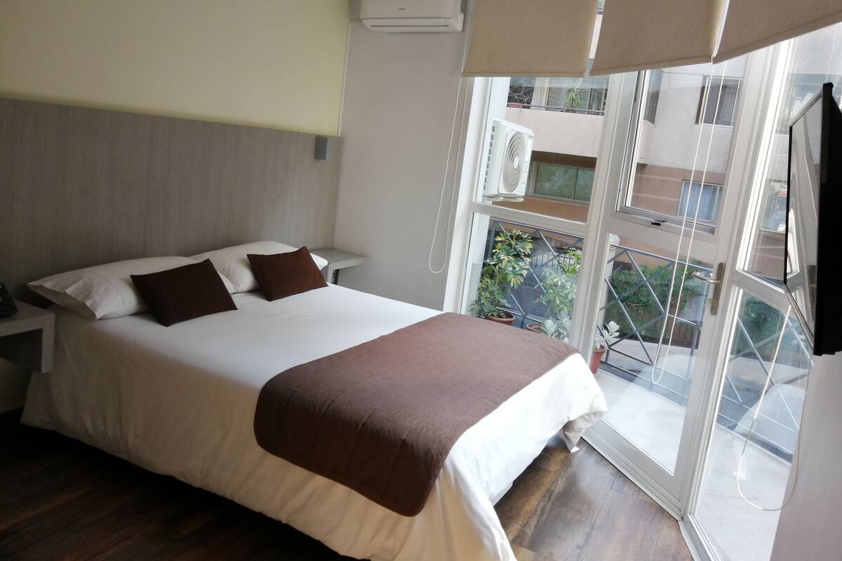 Ein Hotelzimmer mit Bett, Nachttischen, Klimaanlage, Fenster mit Ausblick und einem Balkon.