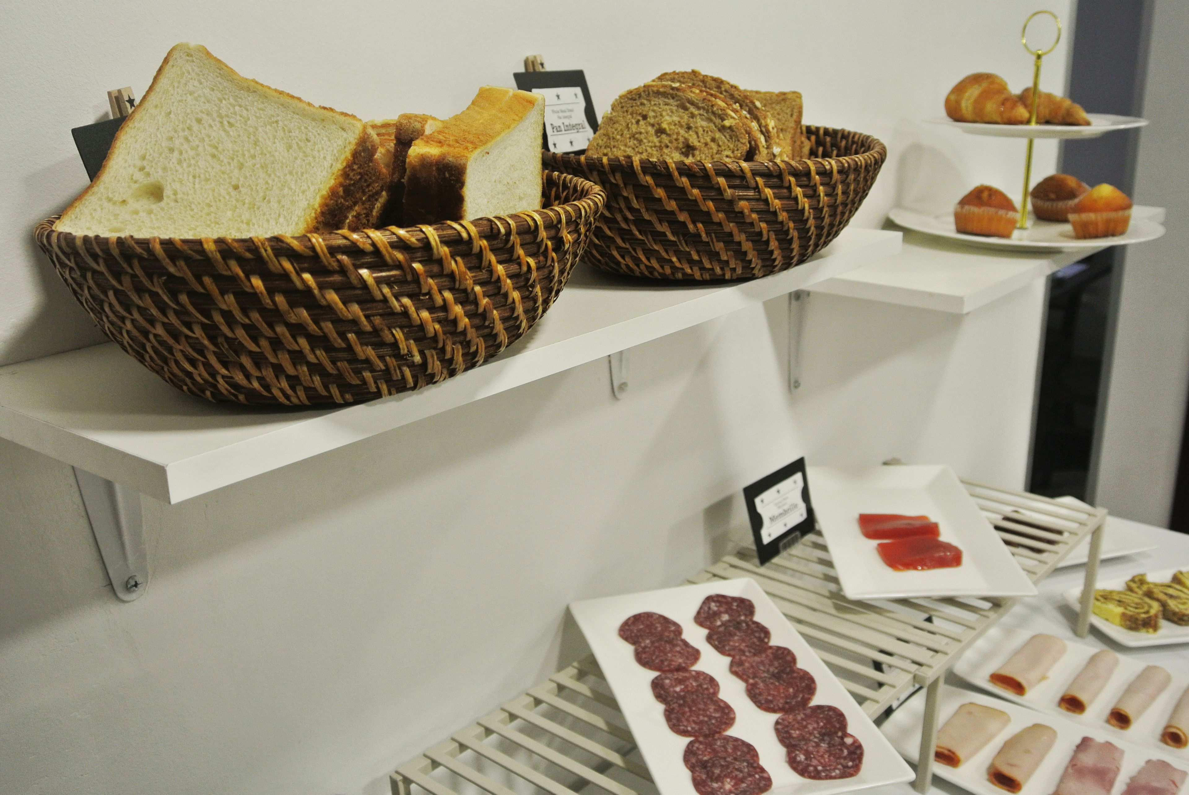 Una exhibición de panes y pasteles sobre una estantería blanca.