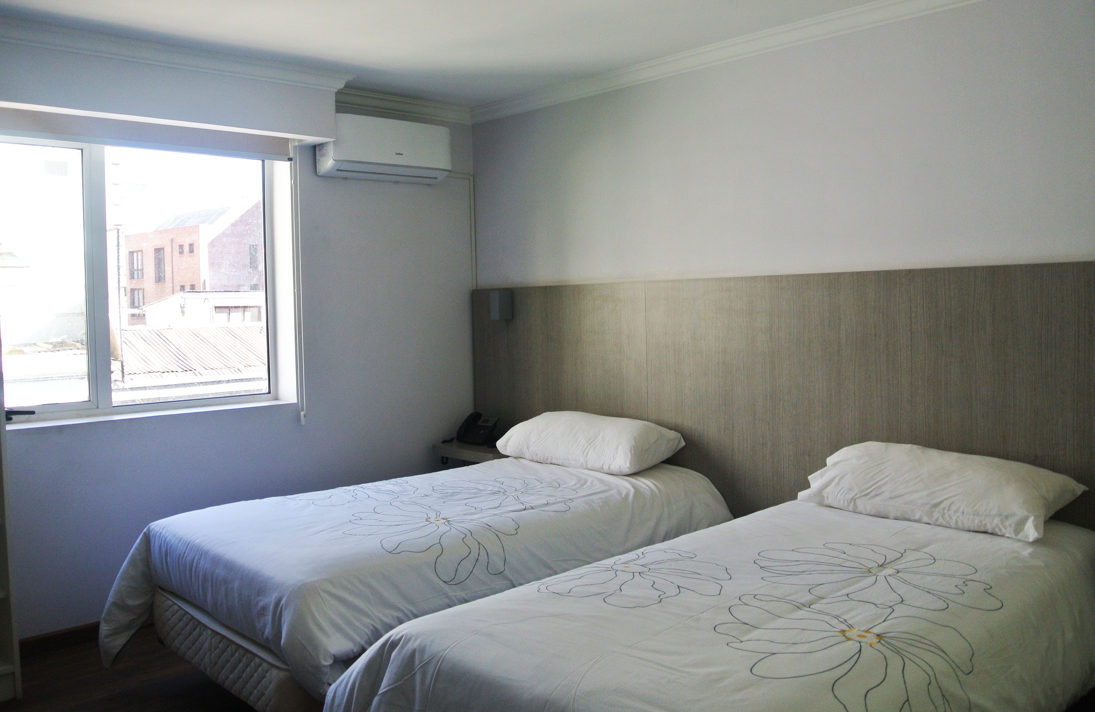 A hotel room with two beds, a window, and an air conditioning unit.