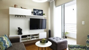 A modern living room with a flat-screen TV, a sofa, an ottoman, and a small table. - UR Place Rentals - 3Bdrm Av Brasil Lima (Lima)