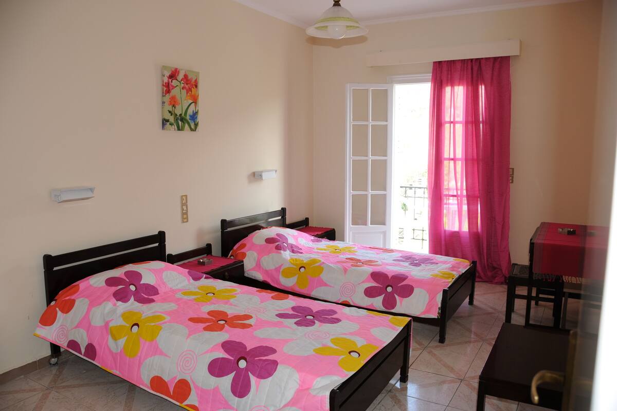 A bedroom with two beds, a small table, and a window with curtains.