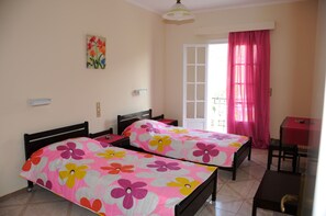 A bedroom with two beds, a small table, and a window with curtains. - Vicky's Garden (Zakynthos)
