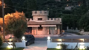A paved driveway leading to a stone building with a tiled roof, surrounded by a well-maintained lawn and street lamps. - Vicky's Garden (Zakynthos)