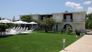A two-story building with a balcony, outdoor seating area with umbrellas, and a well-maintained lawn. - Vicky's Garden (Zakynthos)
