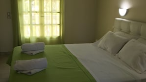 A neatly made bed with a green bedspread and white linens, a window with sheer curtains, and a wall-mounted light fixture. - Vicky's Garden (Zakynthos)