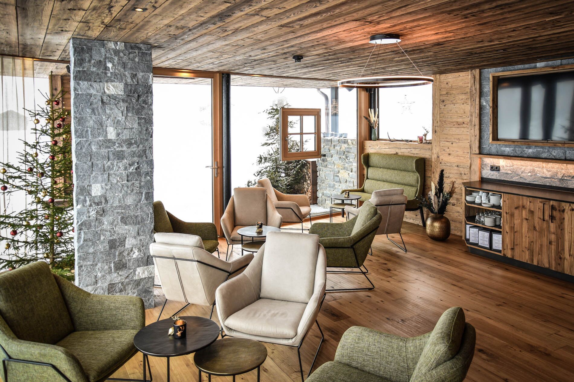 A cozy interior with stone walls, wooden floors, and a mix of green and beige upholstered chairs.