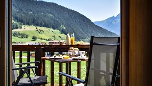 A balcony with a table set for breakfast, overlooking a mountainous landscape.
