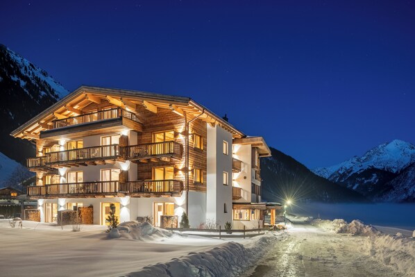 A multi-story hotel with balconies, located near a snow-covered mountain. - NATURPARKGUT - alpdeluxe Apartments (Holzgau)