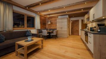 A modern kitchen with wooden beams, a dining area with a table and chairs, and a sofa with a coffee table.