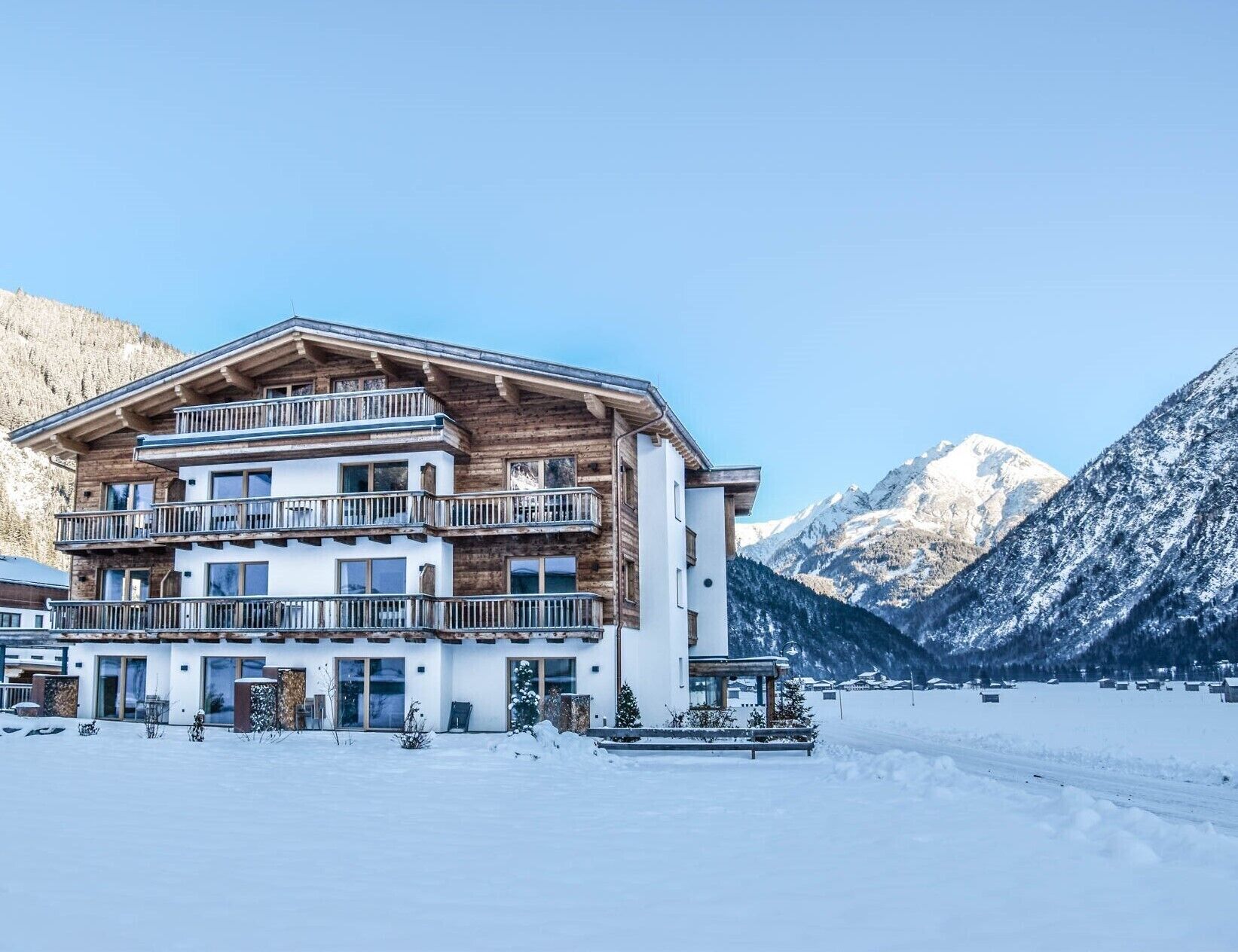 A multi-story hotel with balconies, set against a snowy mountain backdrop.