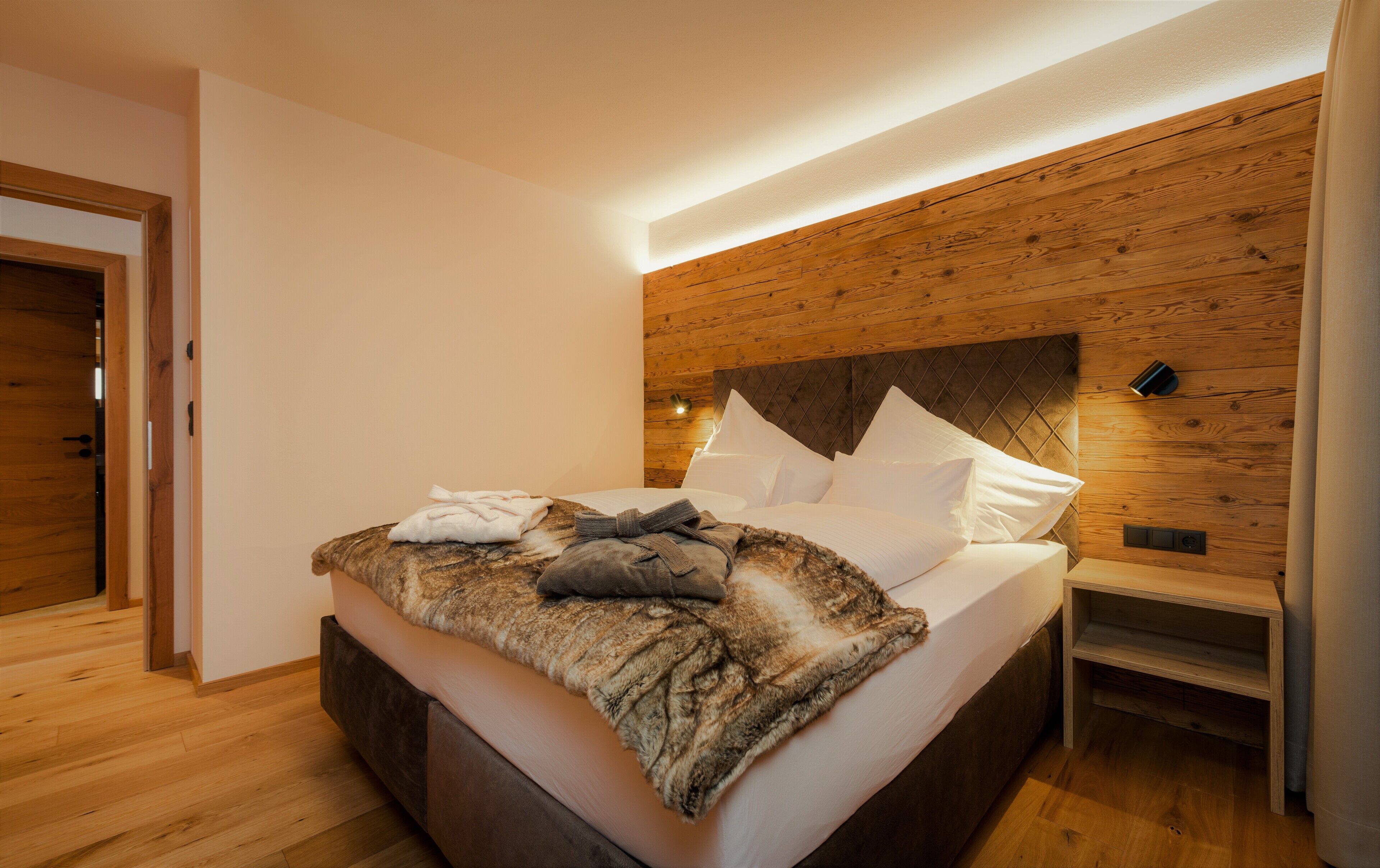 Ein modernes Schlafzimmer mit einem Holzkopfteil, einem Bett mit weißen Leinen und einer flauschigen Decke.