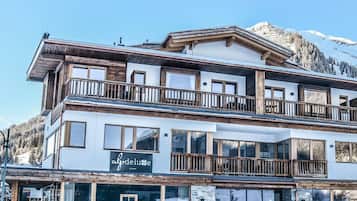 A multi-story hotel with balconies and large windows, set against a mountainous backdrop.