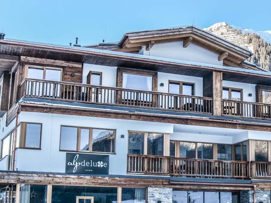 A multi-story hotel with balconies and large windows, set against a mountainous backdrop.