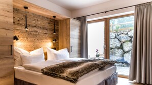 A modern bedroom with a large bed, wooden wall paneling, and a stone wall view.